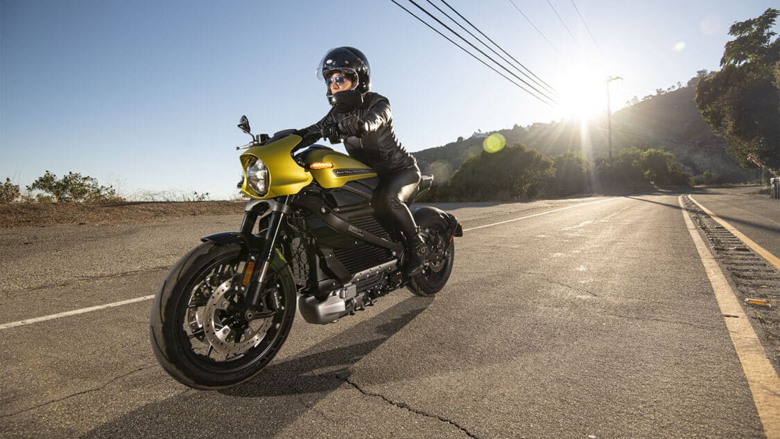 photo of a man or woman wearing protective gear riding a gold and black electric motorcycle on paved road
