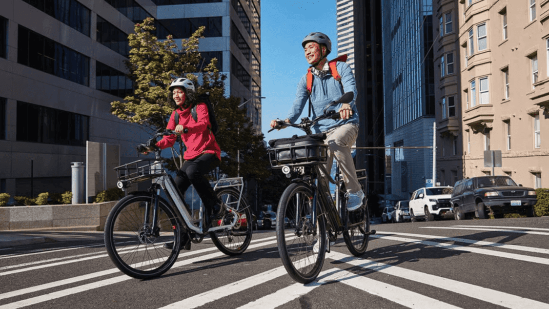 photo of woman and man wearing helmets riding electric bikes on paved road in the city