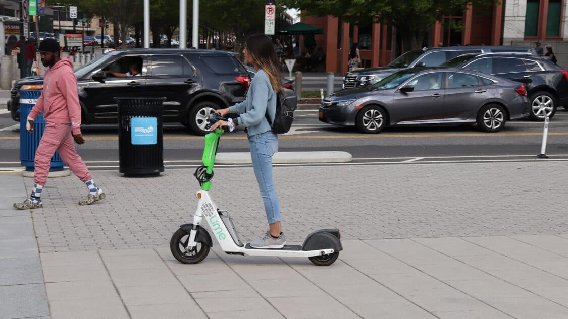 photo of woman riding lime electric scooter e-scooter on sidewalk