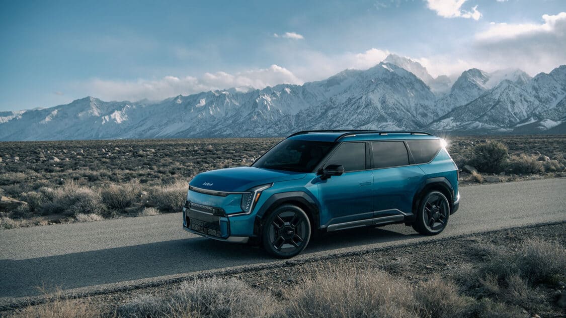 Kia 2024 EV9 SUV blue exterior on the road mountains in the distance