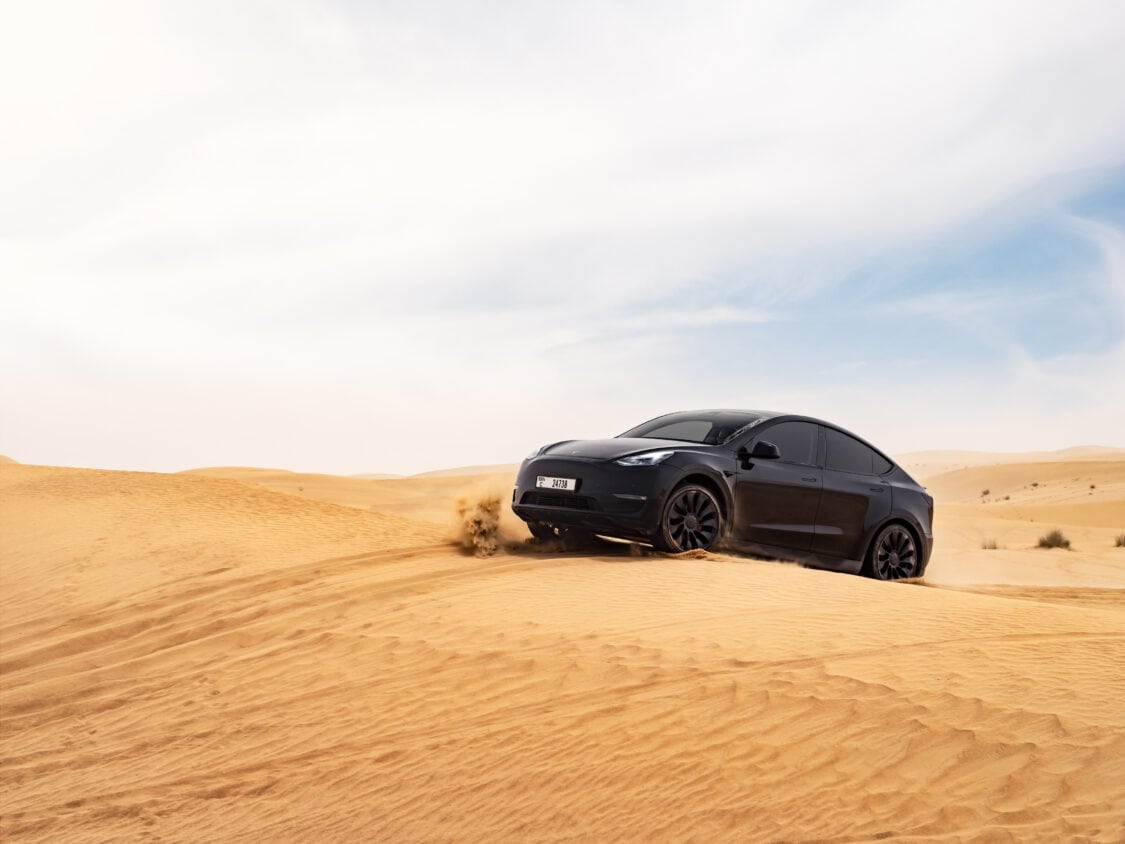 Photo of 2023 Tesla Model Y front 3/4 view, driving up a sand hill