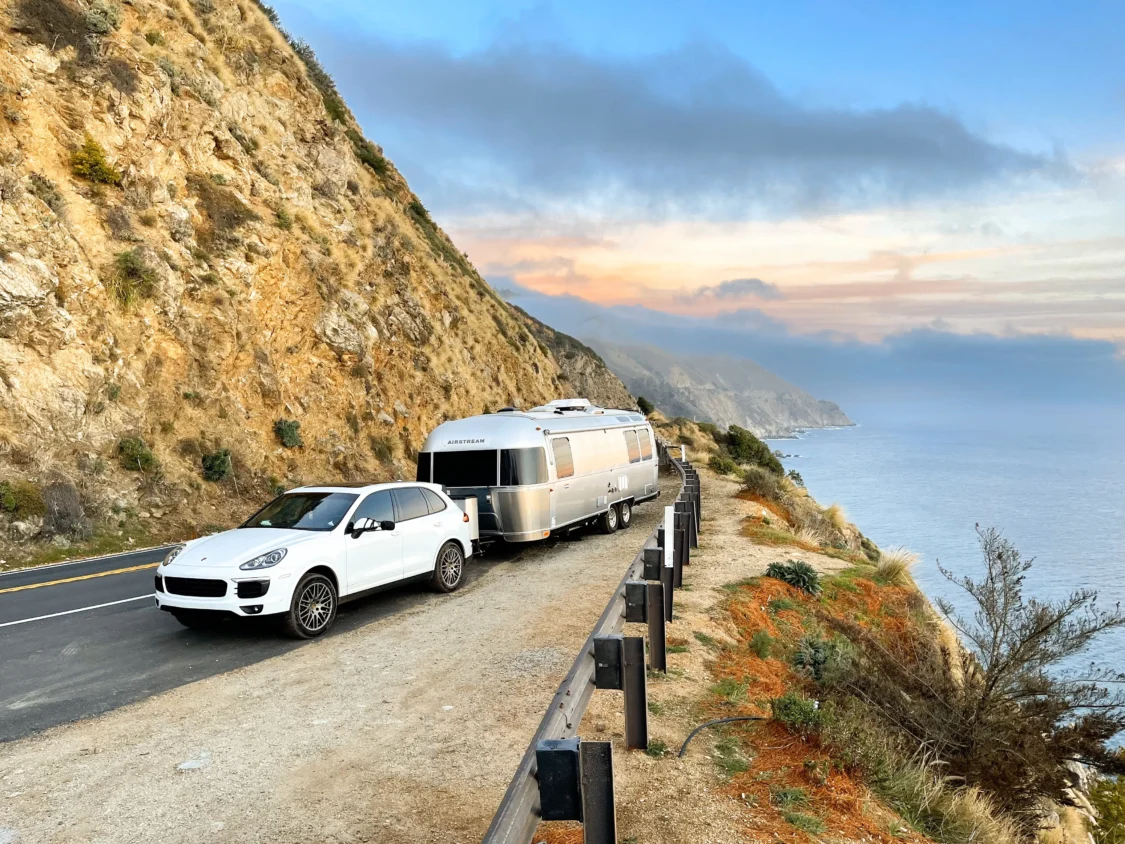 Photo of Porsche Cayenne towing Airstream, parked on a paved street, mountainside and by the ocean