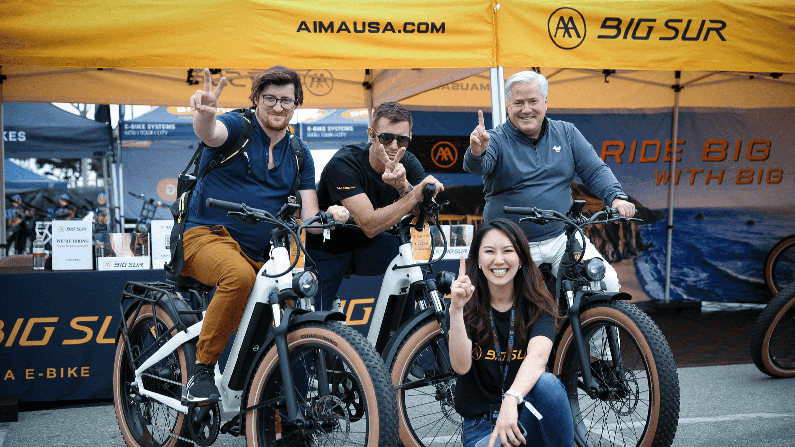 Photo of Electrify Expo attendees test riding the Big Sur matte black electric bike at the AIMA booth.