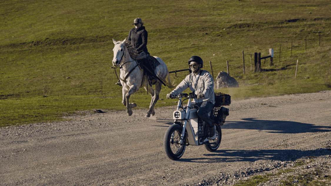 Photo of ASYNC A1 PRO silver electric bike, man riding on dirt road in the country next to a man on a horse