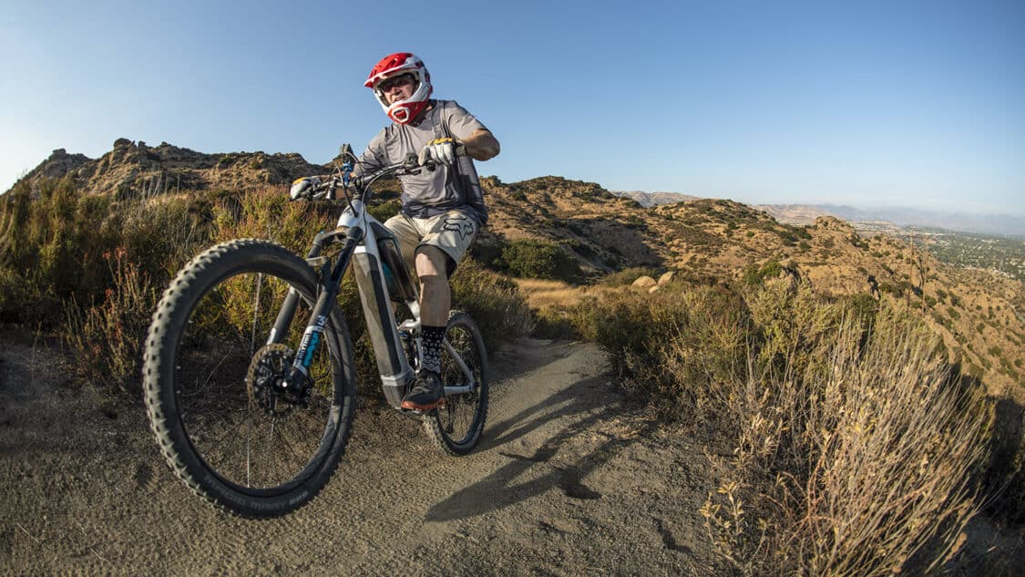 Man wearing a helmet pops a wheelie on an electric bike on a desert hill