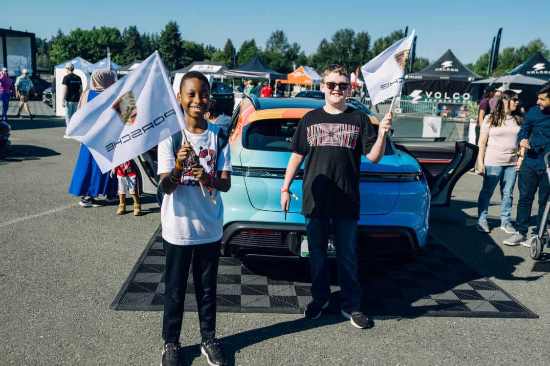 Image showcasing kids holding Porsche flags behind a Porsche Taycan at Electrify Expo Seattle