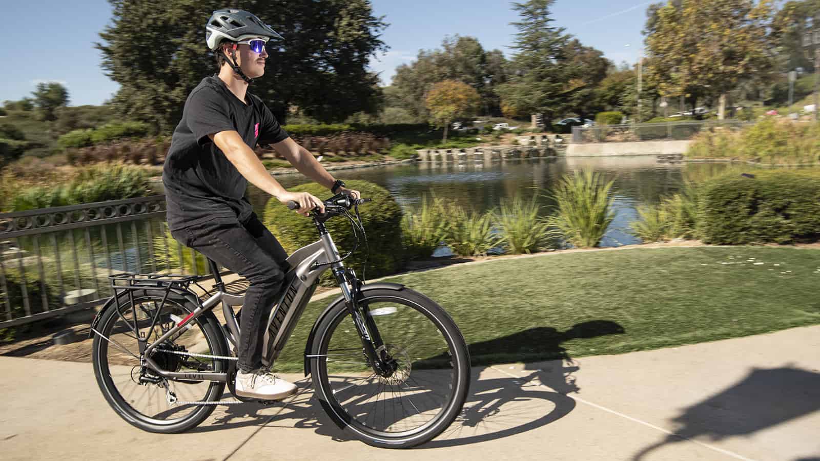 Man wearing black shirt and pants, riding an E-bike with a pond in the background