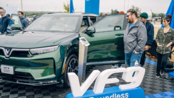 Attendees gather around a green VinFast VF 9 electric SUV at Electrify Expo in Austin, checking out the spacious interior and exterior design up close.