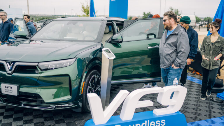 Attendees gather around a green VinFast VF 9 electric SUV at Electrify Expo in Austin, checking out the spacious interior and exterior design up close.