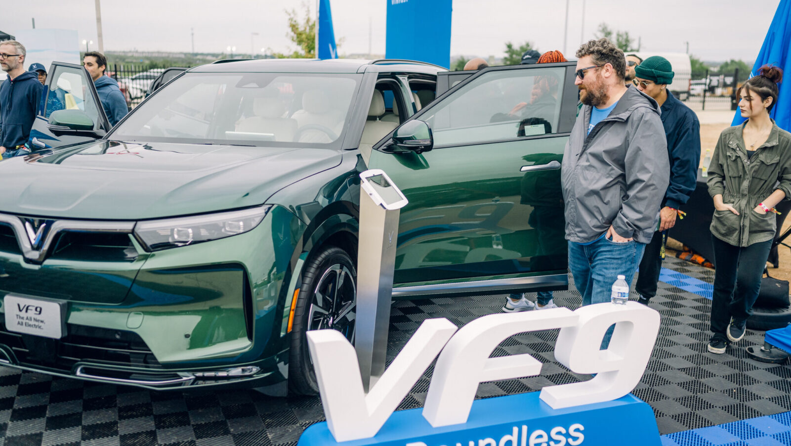 Attendees gather around a green VinFast VF 9 electric SUV at Electrify Expo in Austin, checking out the spacious interior and exterior design up close.