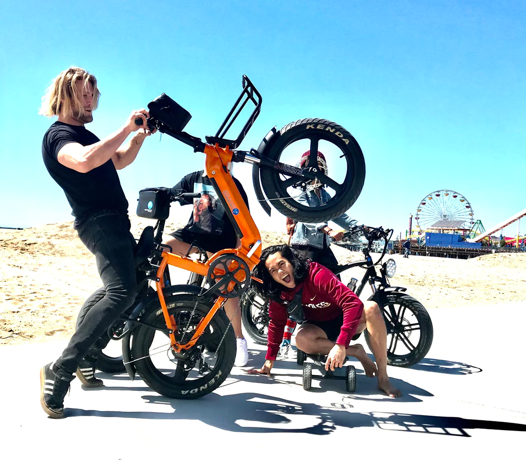 Image showcasing side profile with male riders of the Tripper Electric Bikes FoldX Premium Folding electric bike in custom orange and black