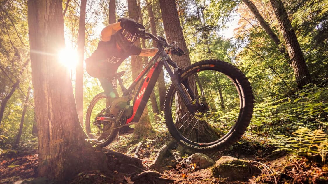 LMX eMTB with rider jumping between trees in dense forest
