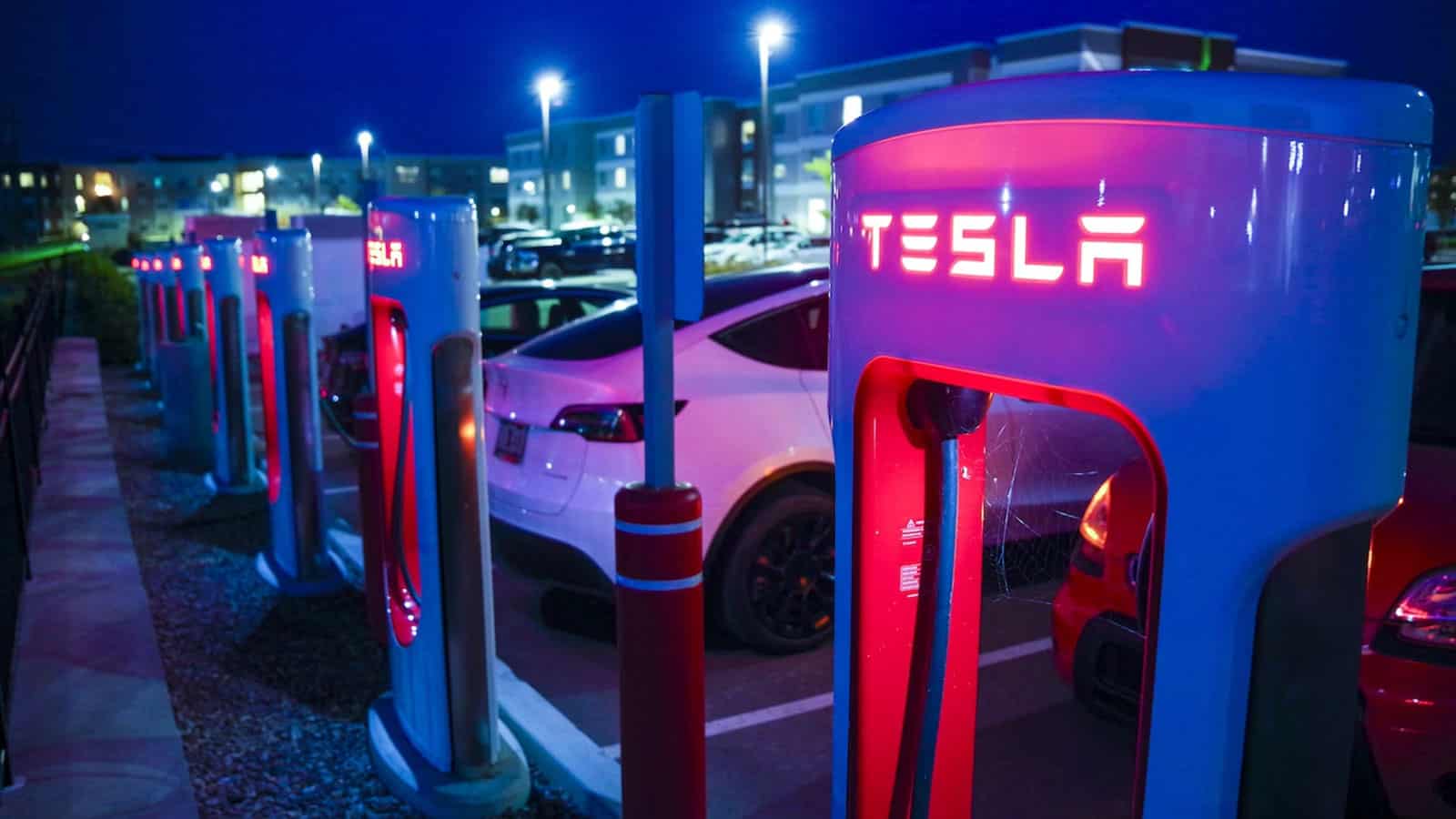 TESLA supercharger row in parking lot, glowing red with blue twilight sky