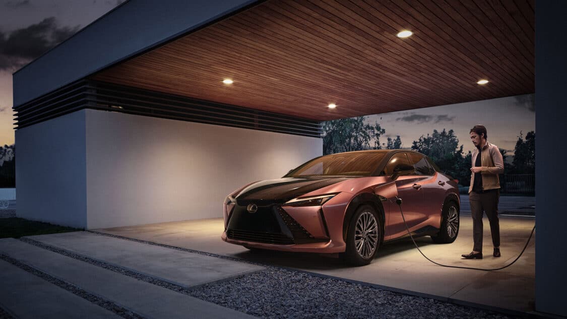 Lexus RZ charging in modern covered parking space with man standing next to it