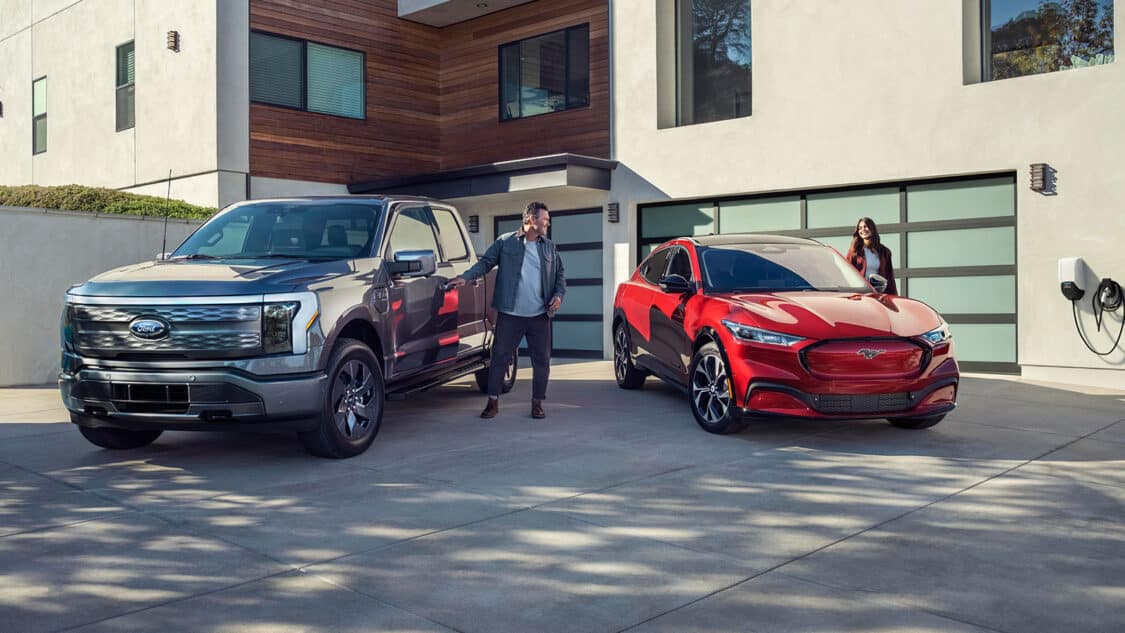 Ford EVs the F-150 Lightning and Mustang Mach-E parked in driveway with man and woman next to driver side doors