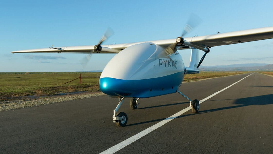 Pyka Pelican Cargo electric plane is parked on a runway, featuring long wings with spinning propellers on the tips
