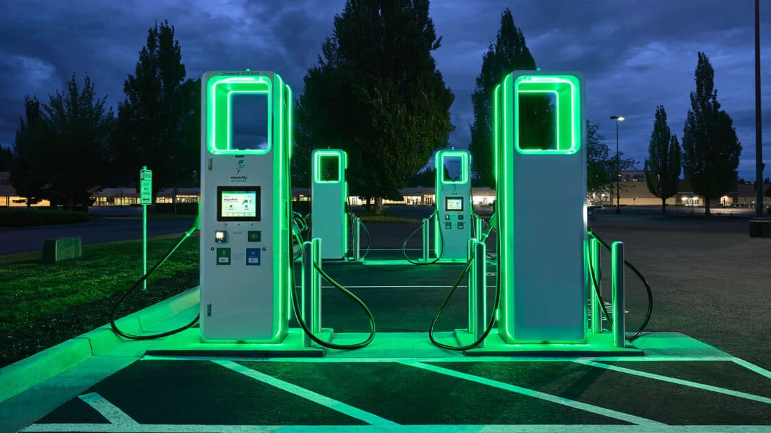 Electrify America EV charging station at night with glowing green lights on charger design