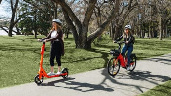 Neuron Mobility scooter and electric bike, with swappable batteries, ridden by women on a treed path