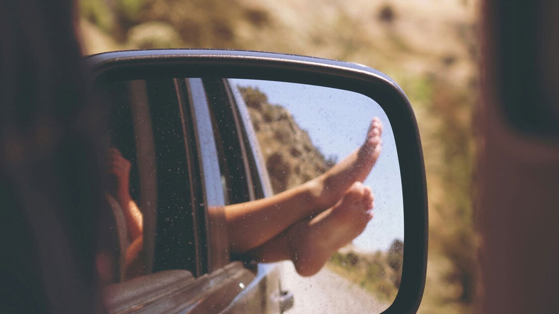 rearview mirror with reflection of feet hanging out rear window on a weekend road trip