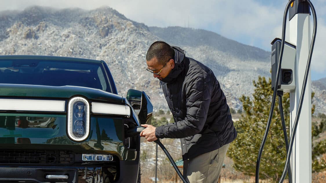Rivian Adventure Network, man plugging in EV with mountain in background