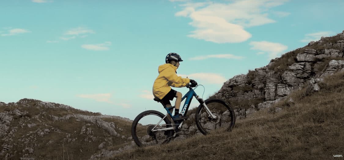 woom showing how it's one of the best electric bikes for kids with boy riding up a mountain