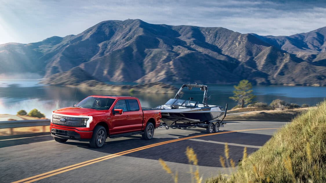 Ford F-150 Lightning driving next to mountain lake pulling a boat