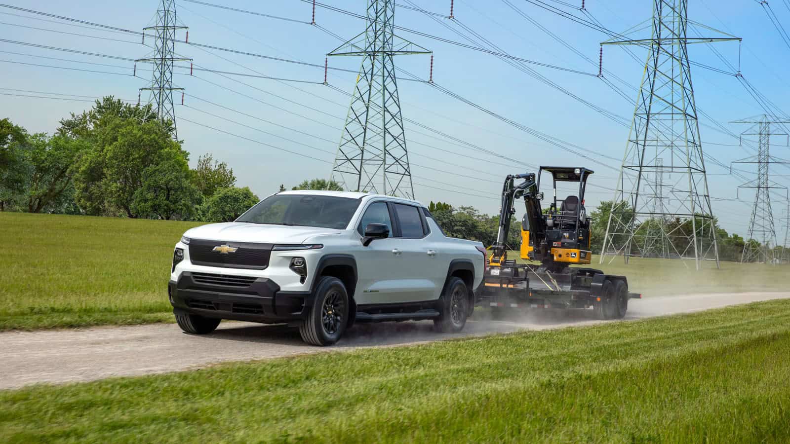 The Chevrolet Silverado EV WT kicking up dust while towing heavy machinery.