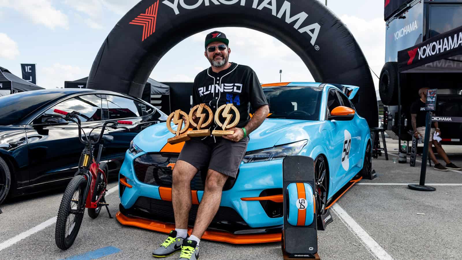 Jason Halvorsen holds awards next to his 2021 Ford Mustang Mach-E GT at Electrify Showoff Orlando 2024