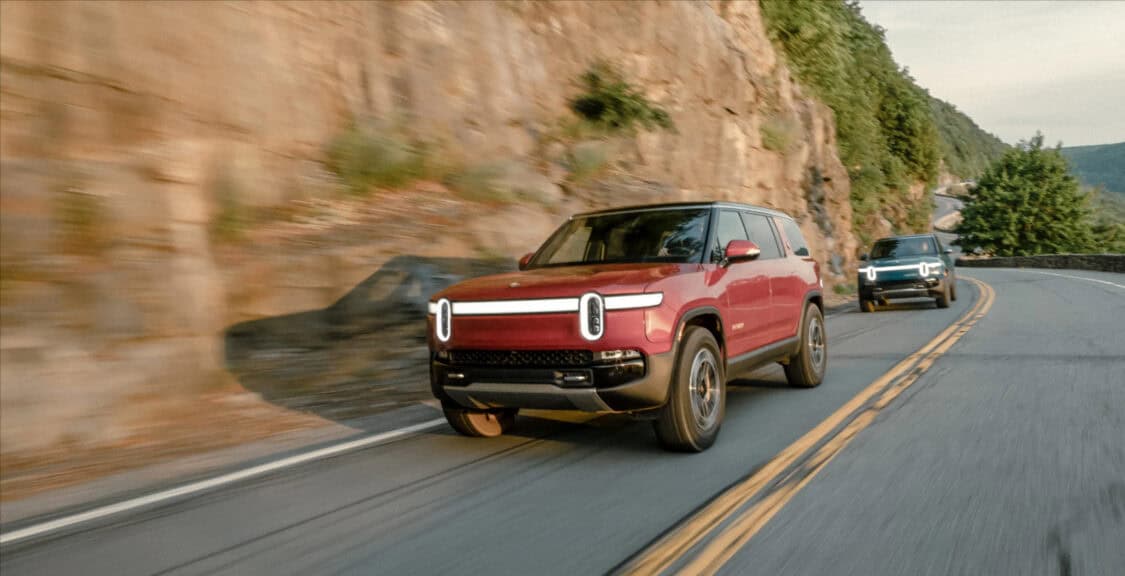 Two Rivian R1S driving next to natural rock wall, EV sales