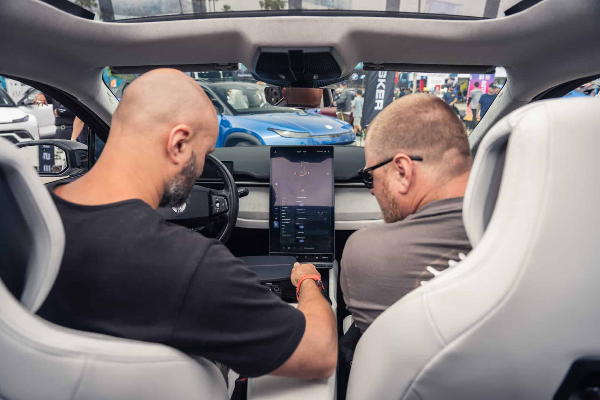 Two individuals interacting with the large touchscreen display inside a Fisker Ocean electric SUV at Electrify Expo.