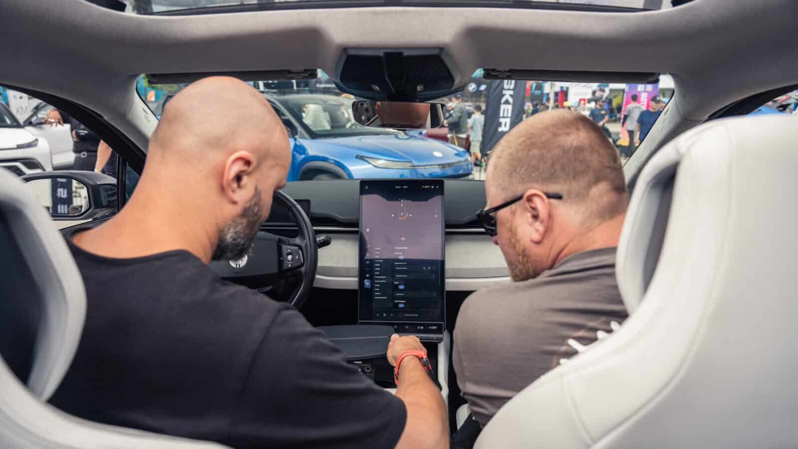 Two individuals interacting with the large touchscreen display inside a Fisker Ocean electric SUV at Electrify Expo.