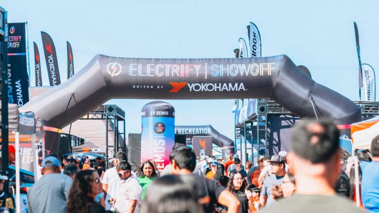 A crowd at Electrify Showoff in Austin under a large Yokohama-branded inflatable archway, surrounded by vendor booths and event banners.