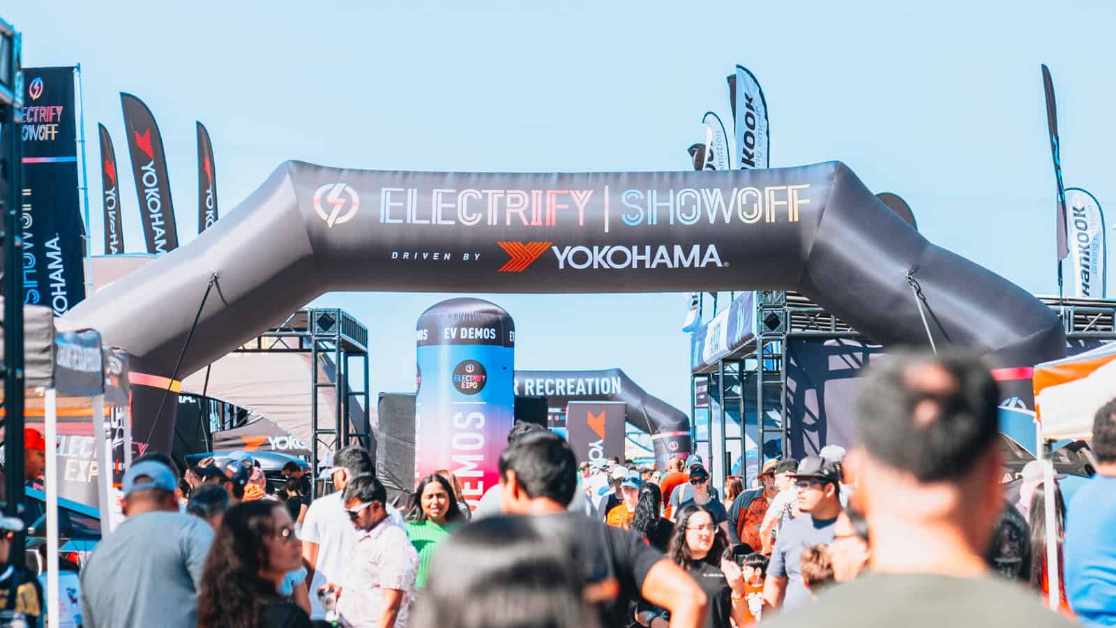 A crowd at Electrify Showoff in Austin under a large Yokohama-branded inflatable archway, surrounded by vendor booths and event banners.