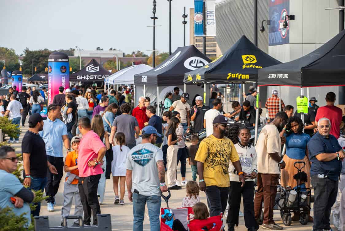 A busy area at Electrify Expo, with attendees exploring vendor tents and engaging with micromobility products and demonstrations.