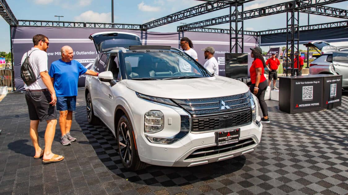 White Mitsubishi Outlander PHEV at Electrify Expo surrounded by attendees and staff engaging with the vehicle