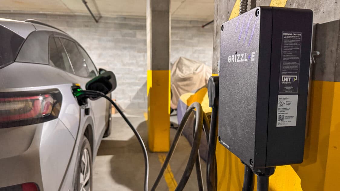 A Volkswagen ID.4 electric vehicle is charging at a Grizzl-E Level 2 charger in an indoor parking garage. The charging cable is plugged into the vehicle, with a green indicator light showing active charging.