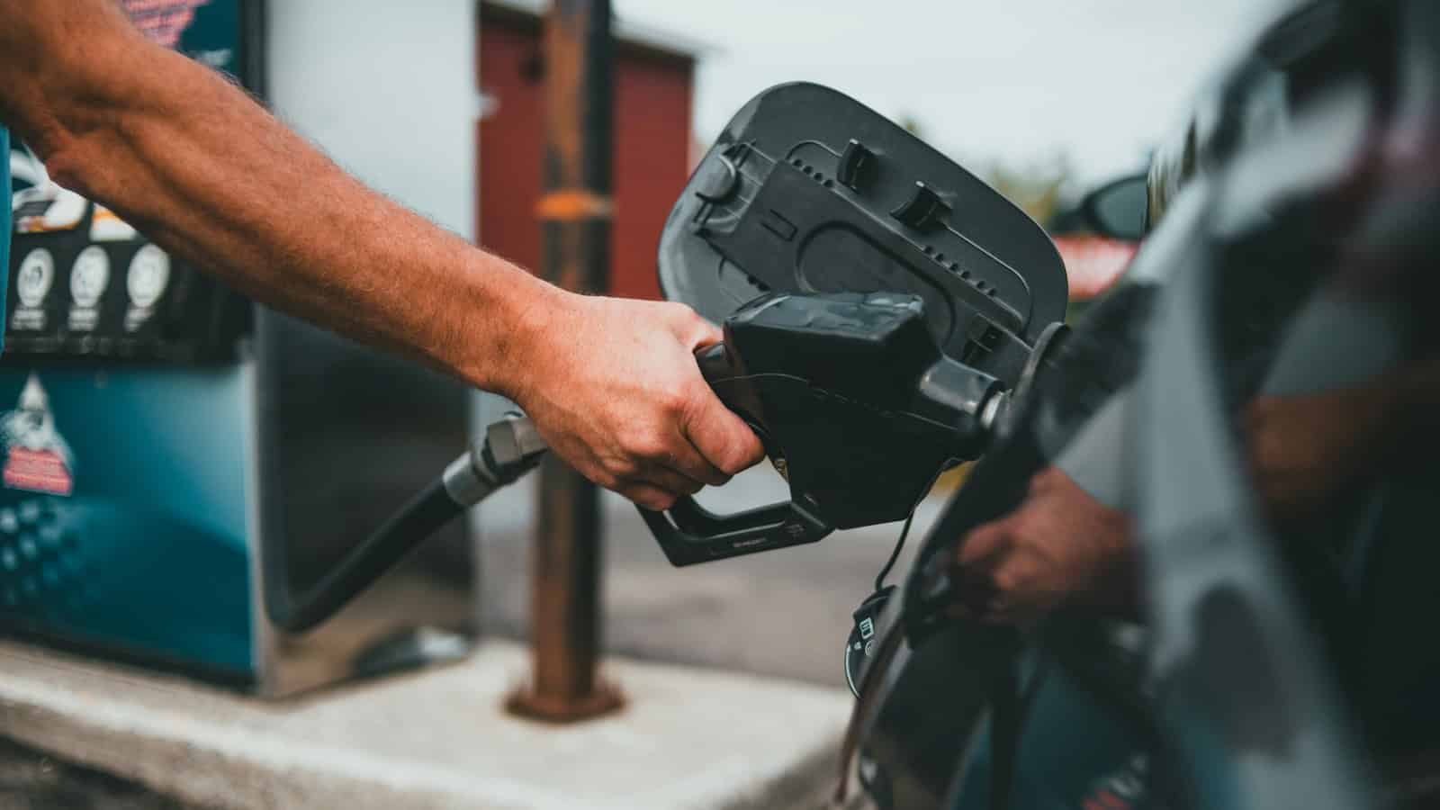 A person refueling a car at a gas station, holding a gas pump handle.