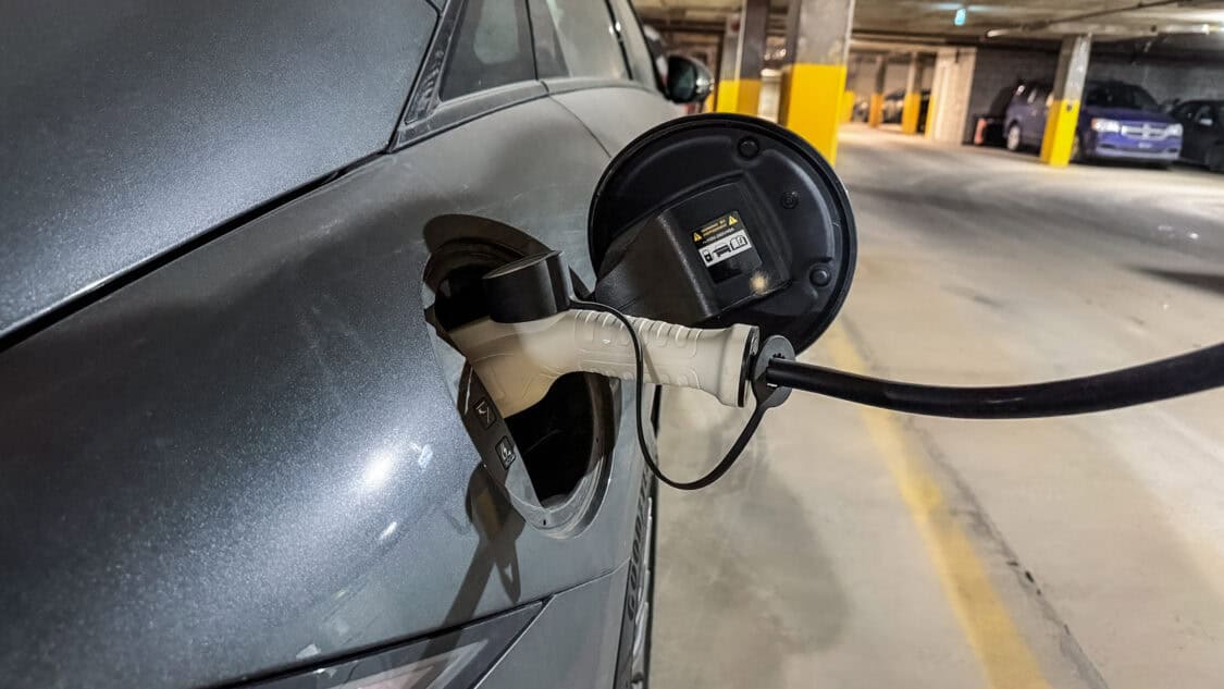 Close-up of a Hyundai Ioniq 6 electric vehicle charging at a home charger in a parking garage.