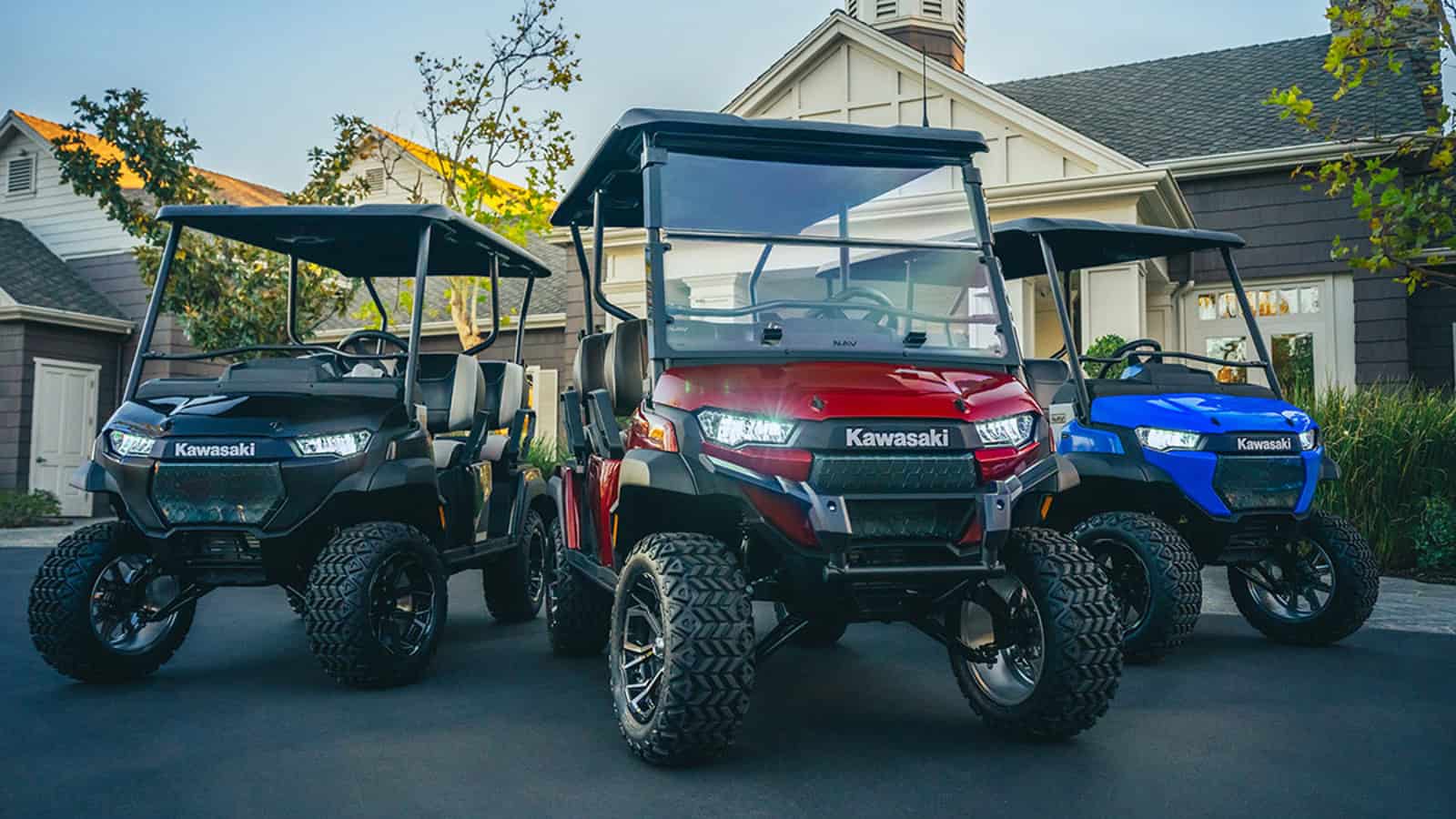 Three Kawasaki NAV 4e electric golf carts in black, red, and blue are parked in a residential driveway, featuring rugged tires, LED headlights, and a modern design.