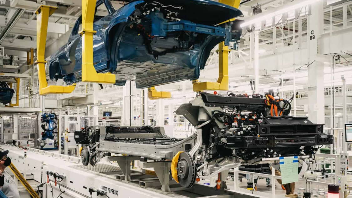 An electric vehicle assembly line showing a Rivian R1T truck body being lowered onto its chassis.