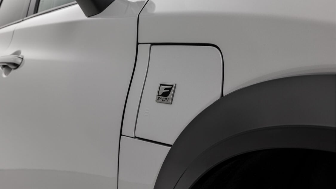 Closeup view of the F SPORT badge a 2026 Lexus RZ 550e F SPORT electric SUV in Wind color, light gray with subtle metallics.