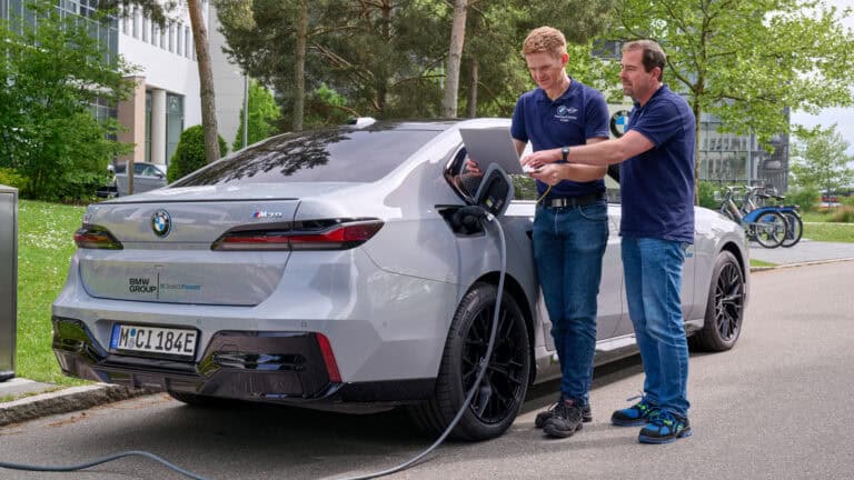 Two engineers charge a BMW i7 test vehicle equipped with a Solid Power all-solid-state battery (ASSB) outside a BMW Group facility.