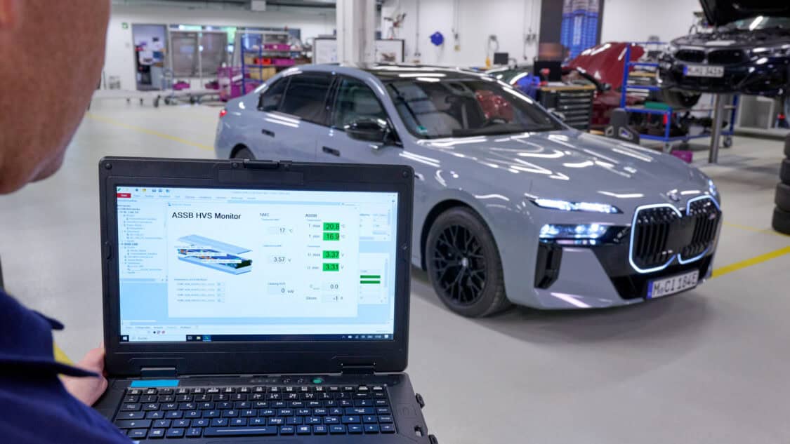 An engineer works on a laptop connected to a BMW i7 test vehicle with Solid Power all-solid-state battery technology inside a BMW Group workshop.
