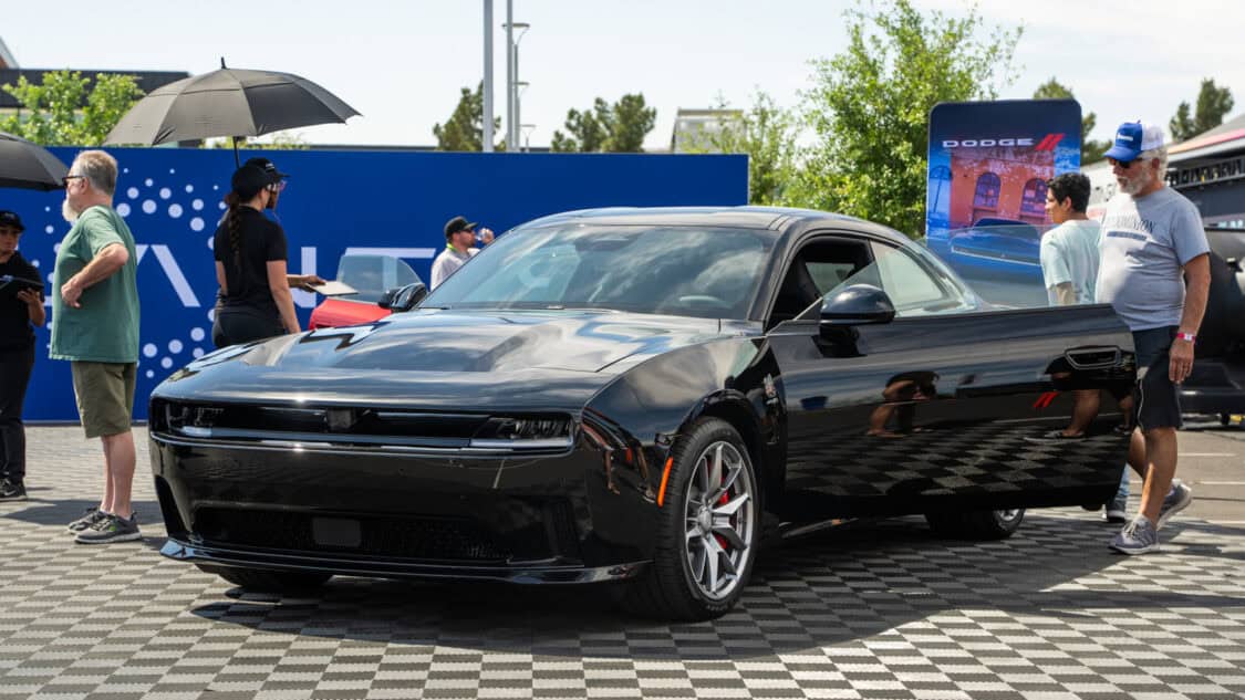 A black Dodge Charger EV electric muscle car is displayed outdoors at the Stellantis booth at Electrify Expo Phoenix.