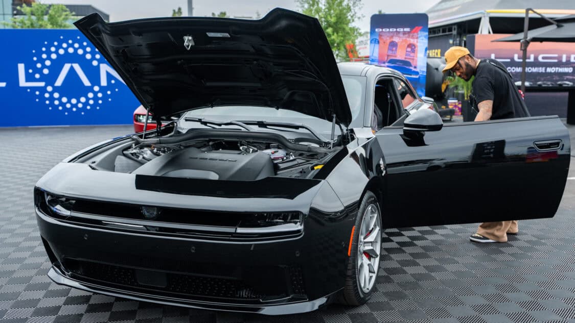 A black Dodge Charger EV electric muscle car is displayed outdoors at the Stellantis booth at Electrify Expo Phoenix.