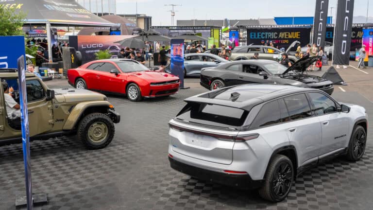 A variety of Dodge and Jeep electric vehicles, including a red Dodge Charger, black Dodge Charger Daytona, silver Wagoneer S, and tan Jeep Wrangler 4xe, are showcased in the Stellantis booth at Electrify Expo Phoenix.