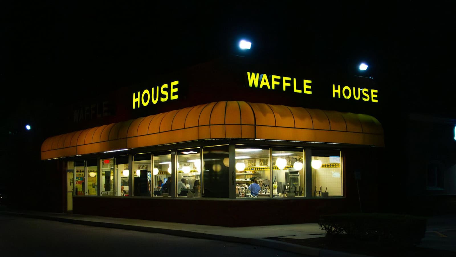 A Waffle House restaurant lit up at night, viewed from outside with people dining inside.