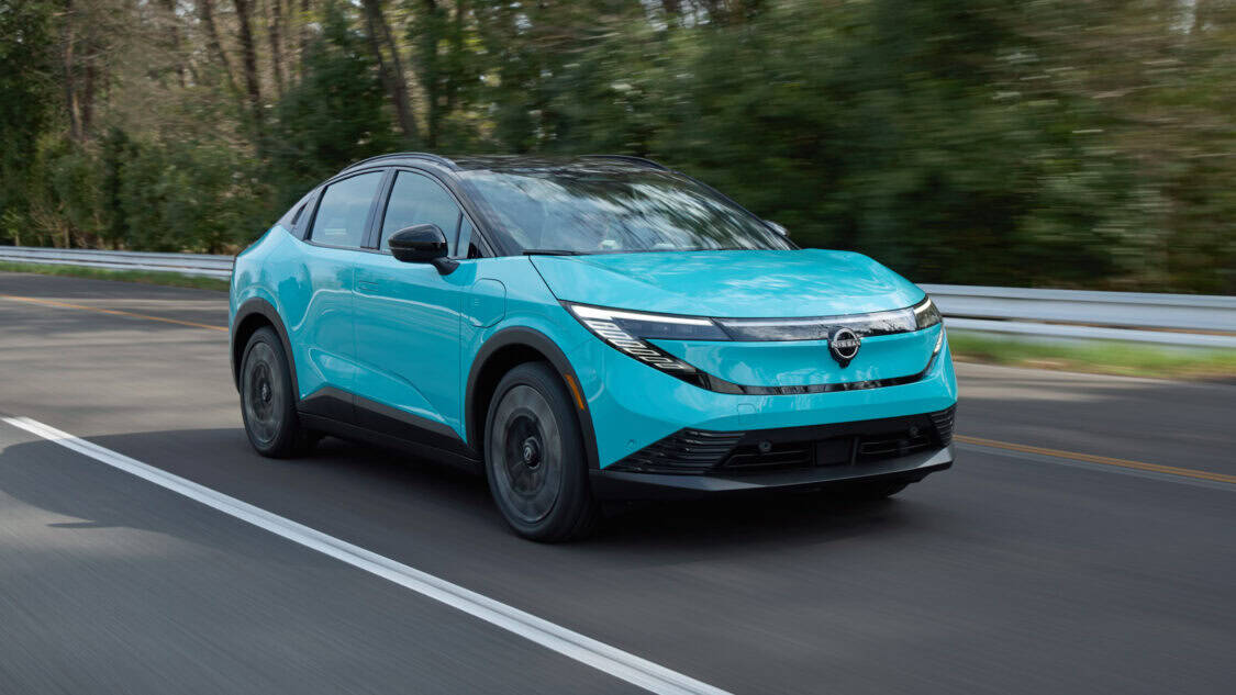 2026 Nissan Leaf compact electric SUV in Seabreeze Blue driving on a forested road, showcasing its new crossover design and updated LED headlights.