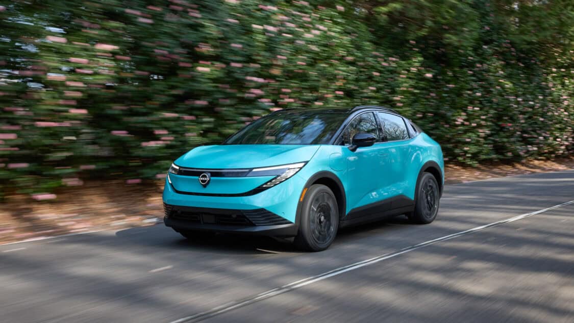 2026 Nissan Leaf compact electric SUV in Seabreeze Blue driving on a forested road, showcasing its new crossover design and updated LED headlights.
