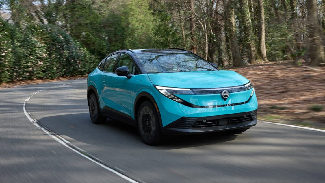 2026 Nissan Leaf compact electric SUV in Seabreeze Blue driving on a forested road, showcasing its new crossover design and updated LED headlights.